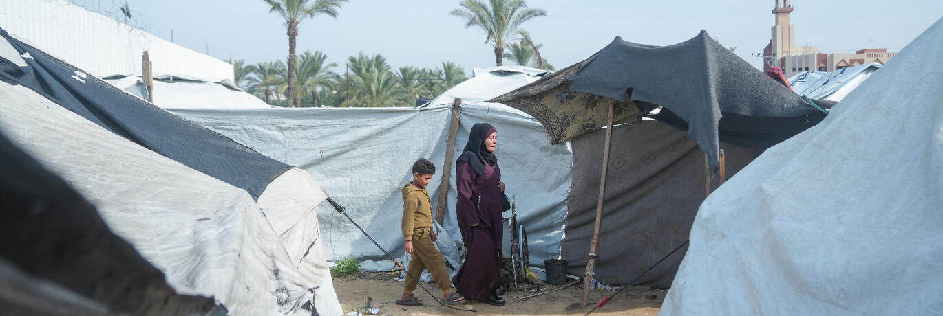 Rawya, een ontvanger van CASH-hulp in Gaza, loopt met haar kinderen door een geïmproviseerd tentenkamp in Gaza