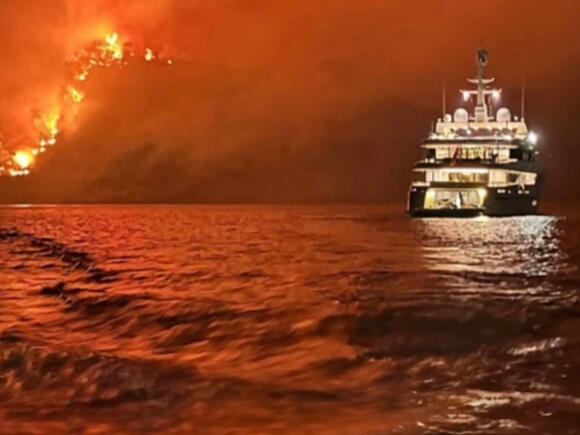 Superyacht against backdrop of fire