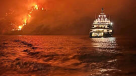 Superyacht against backdrop of fire
