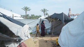 Rawya, een ontvanger van CASH-hulp in Gaza, loopt met haar kinderen door een geïmproviseerd tentenkamp in Gaza